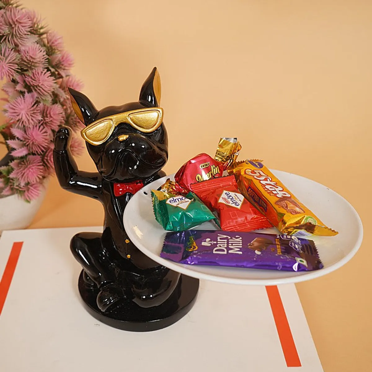 Black figurine with bow tie and sunglasses holding a tray of wrapped sweets