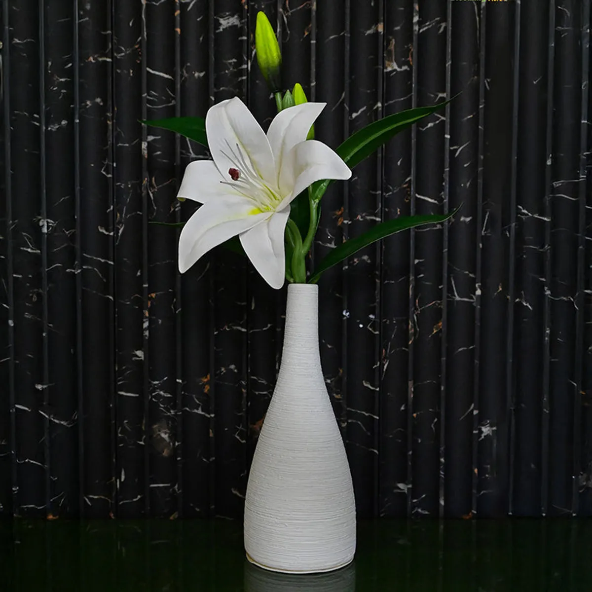 White slender vase with lily stem on a dark textured backdrop