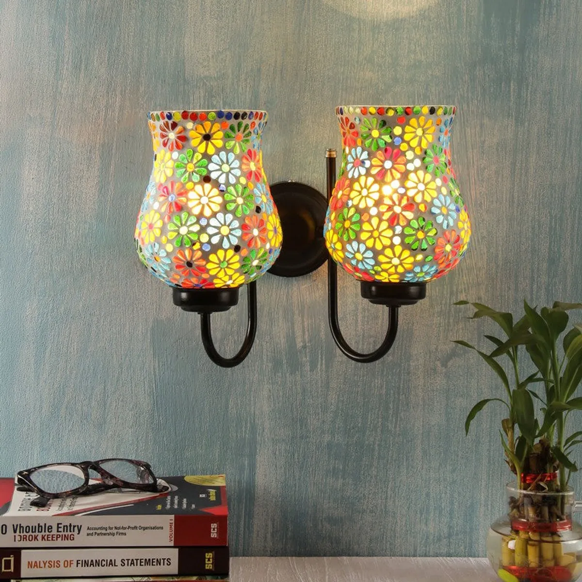 Lit dual floral mosaic wall lamp with black iron base against a blue wall