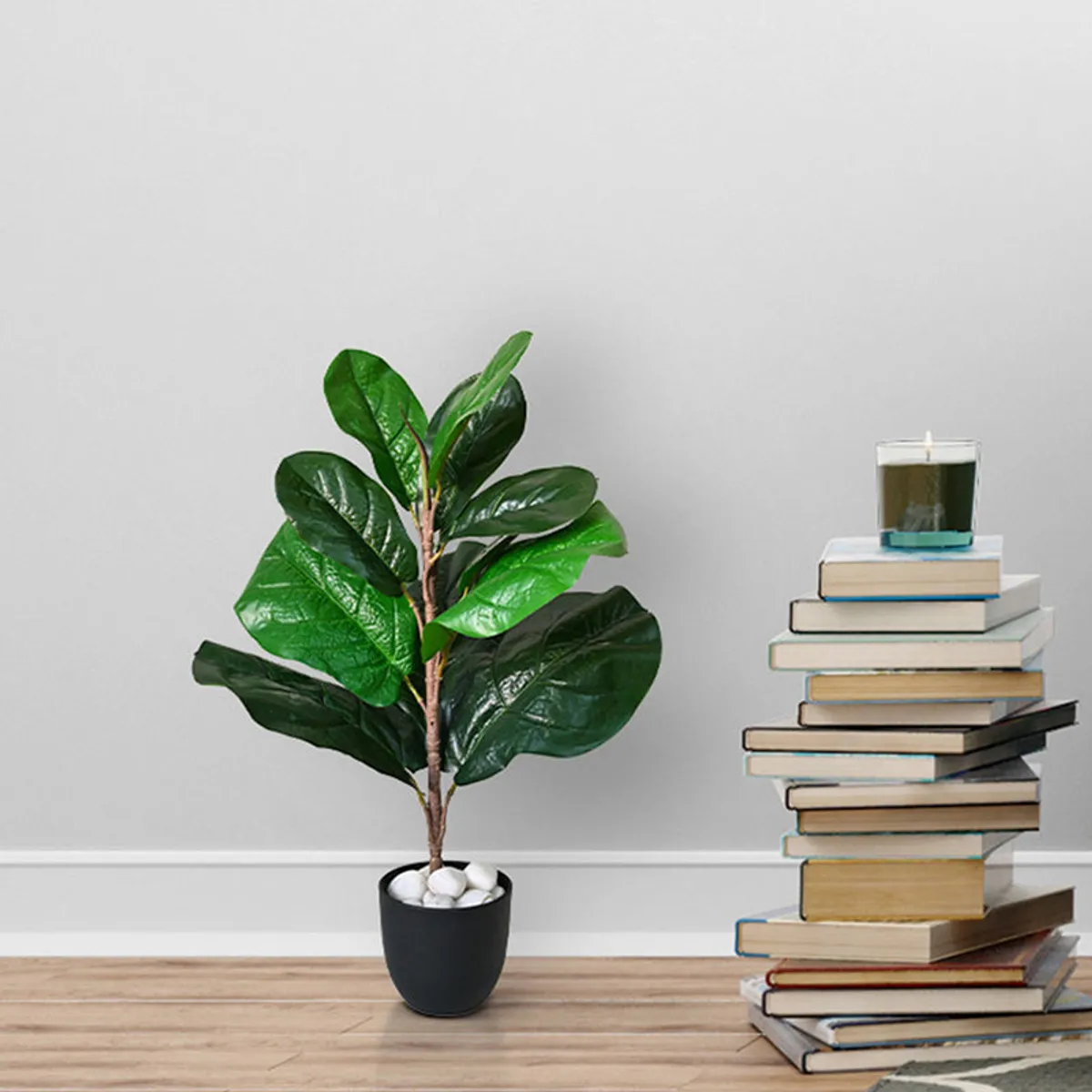 Green artificial fiddle leaf fig plant in a black pot beside a stack of books