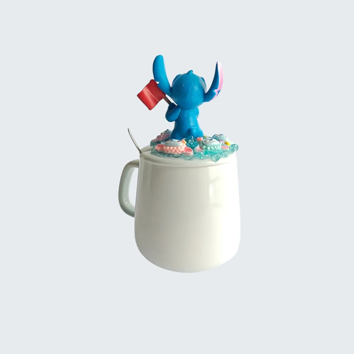 Back view of white mug with blue figurine lid and spoon