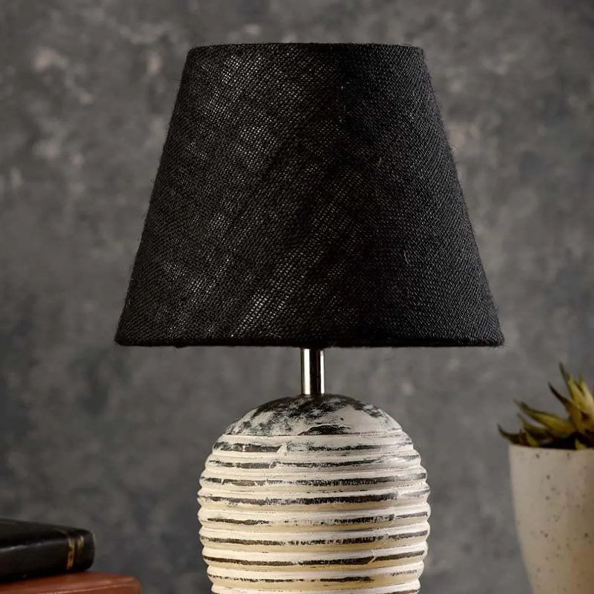 Table lamp with black conical shade and ribbed beige base on a dark backdrop