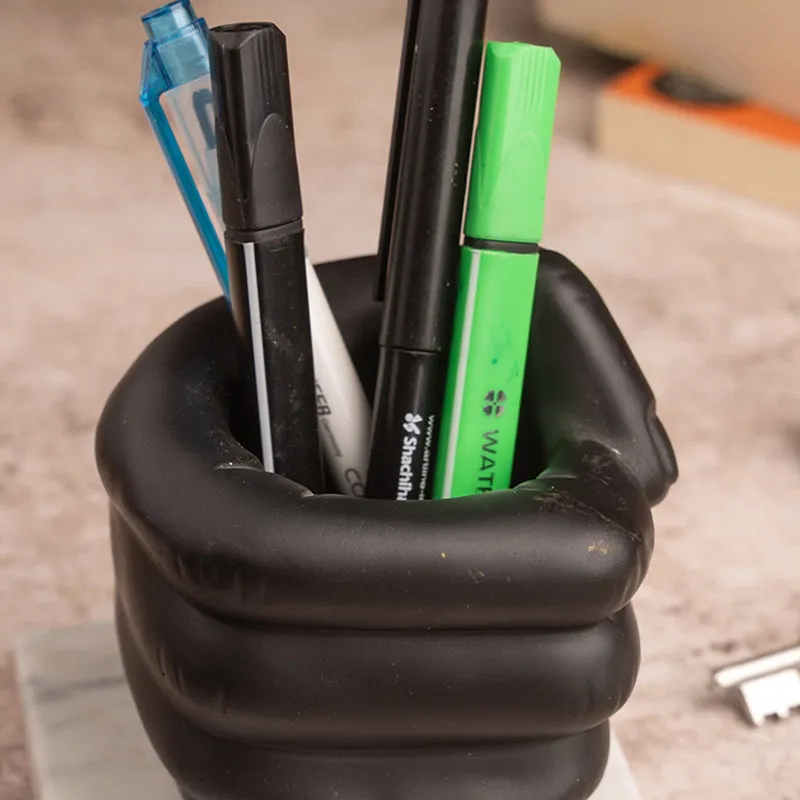 Close-up of black fist-shaped pen stand holding pens