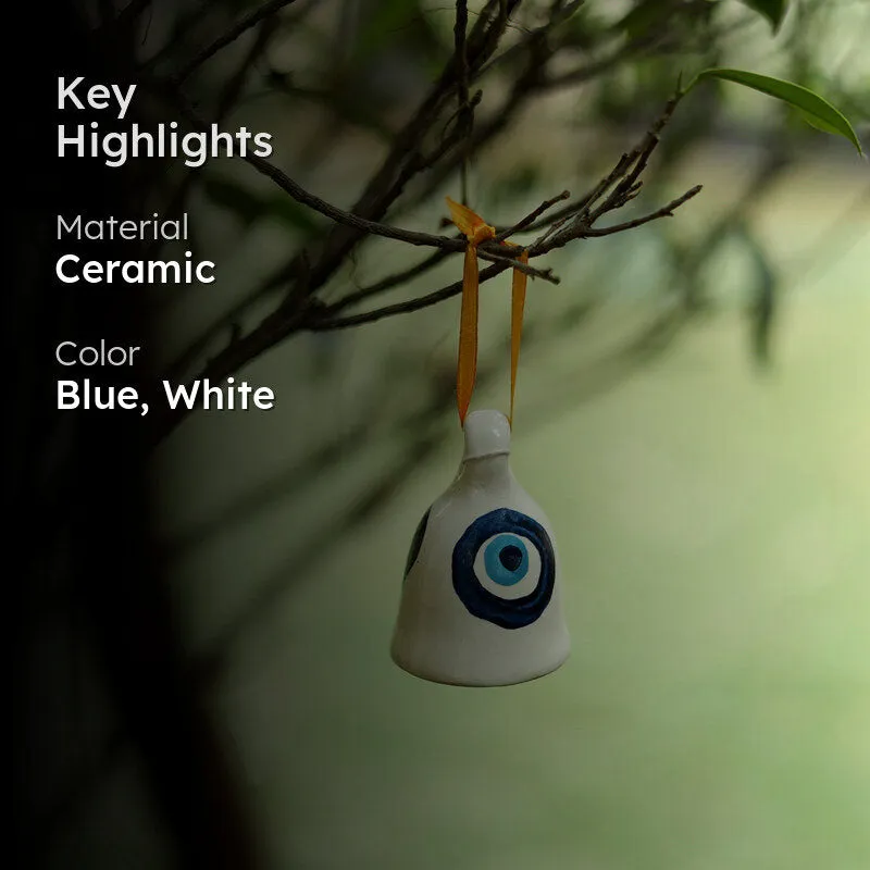 White ceramic hanging bell with blue evil eye motif suspended from a yellow ribbon