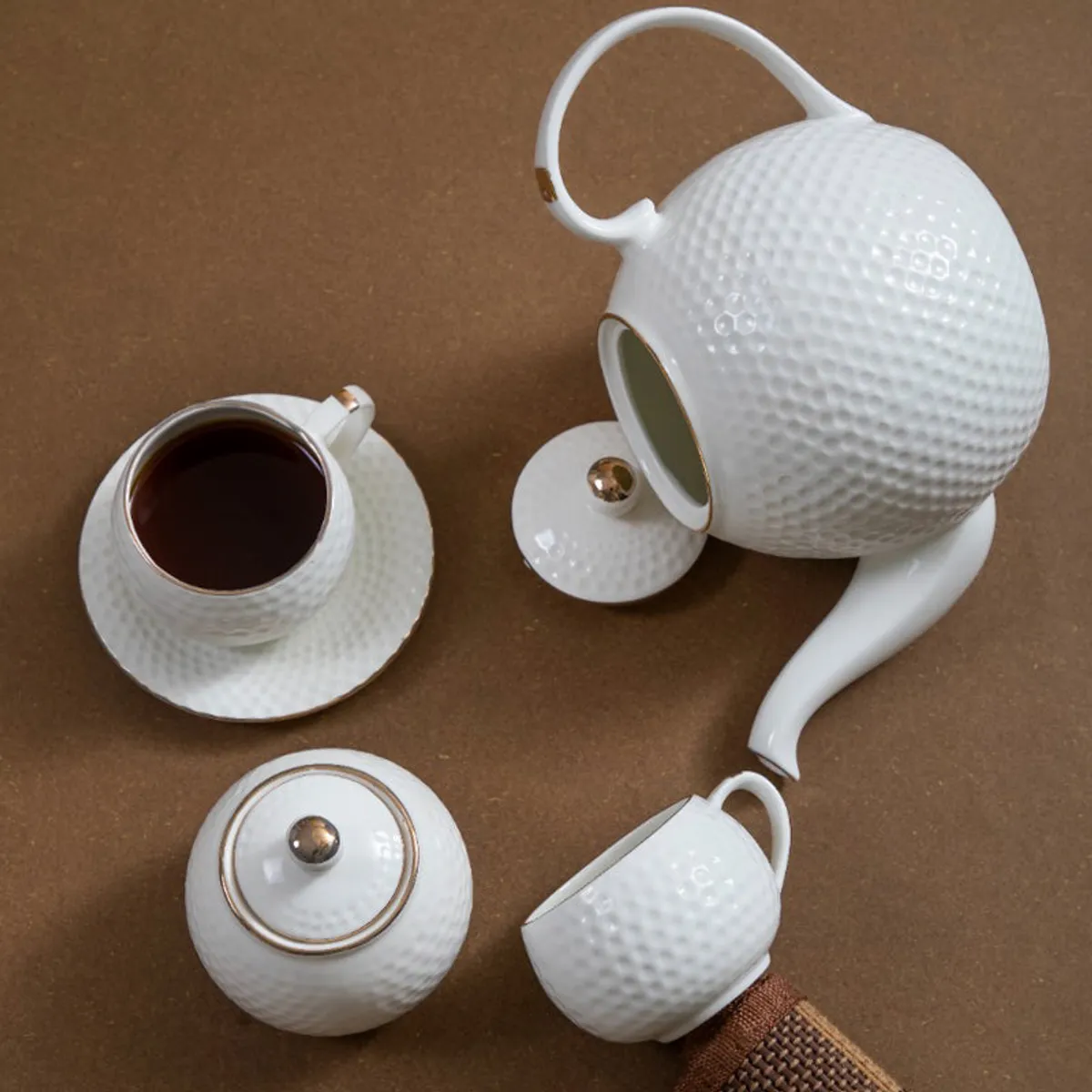 White textured teapot, cup, saucer and serving pieces arranged on a brown surface