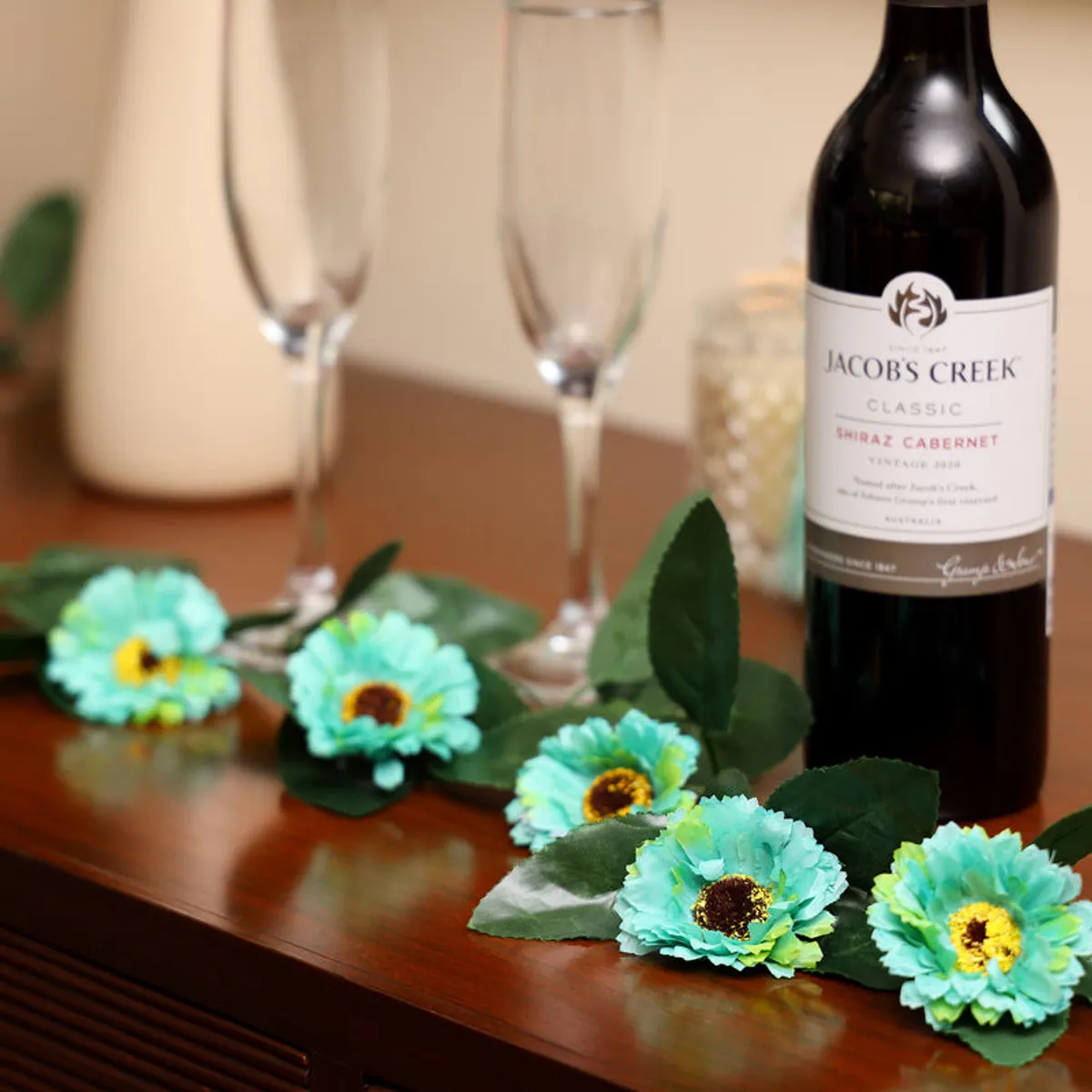 Blue artificial flowers and green leaves styled across a dining table.