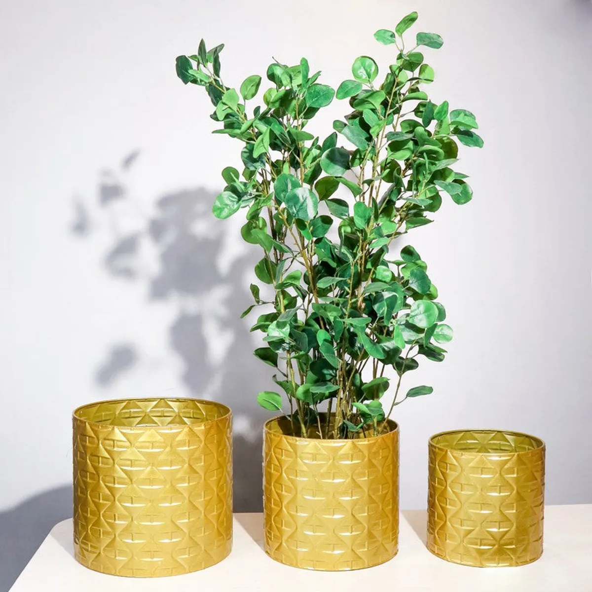 Three gold planters displayed together, with green foliage placed in the centre planter.