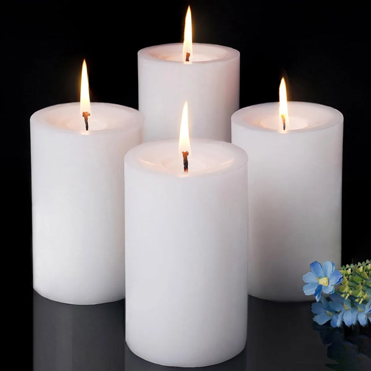 Set of four lit white pillar candles against a black background