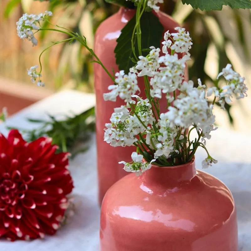Pink ceramic vase with white flowers, with another vase blurred in the background.