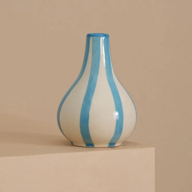 White and blue striped ceramic vase displayed on a beige pedestal