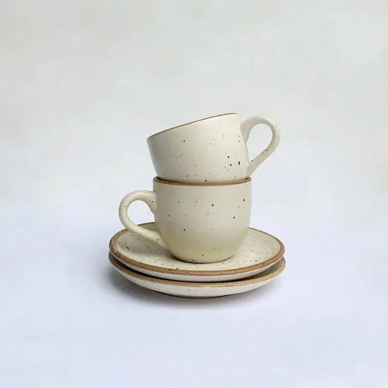 Two white speckled ceramic cups stacked with matching saucers