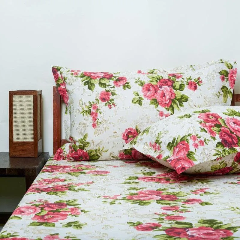 White bedsheet and pillow covers with red rose floral print on a bed