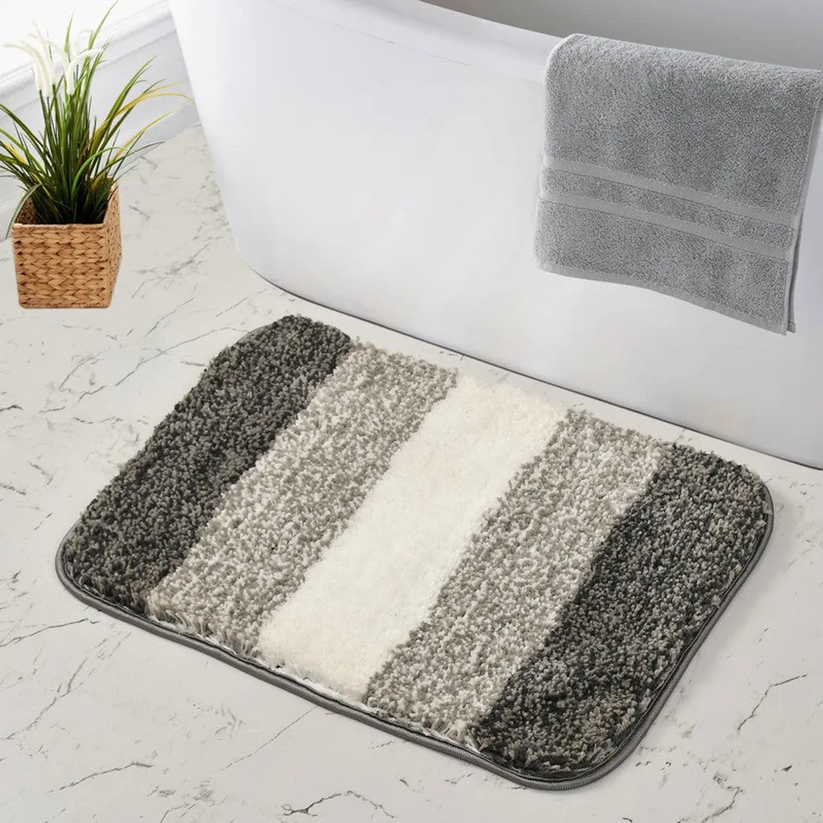 Striped grey and white bath mat placed beside a bathtub