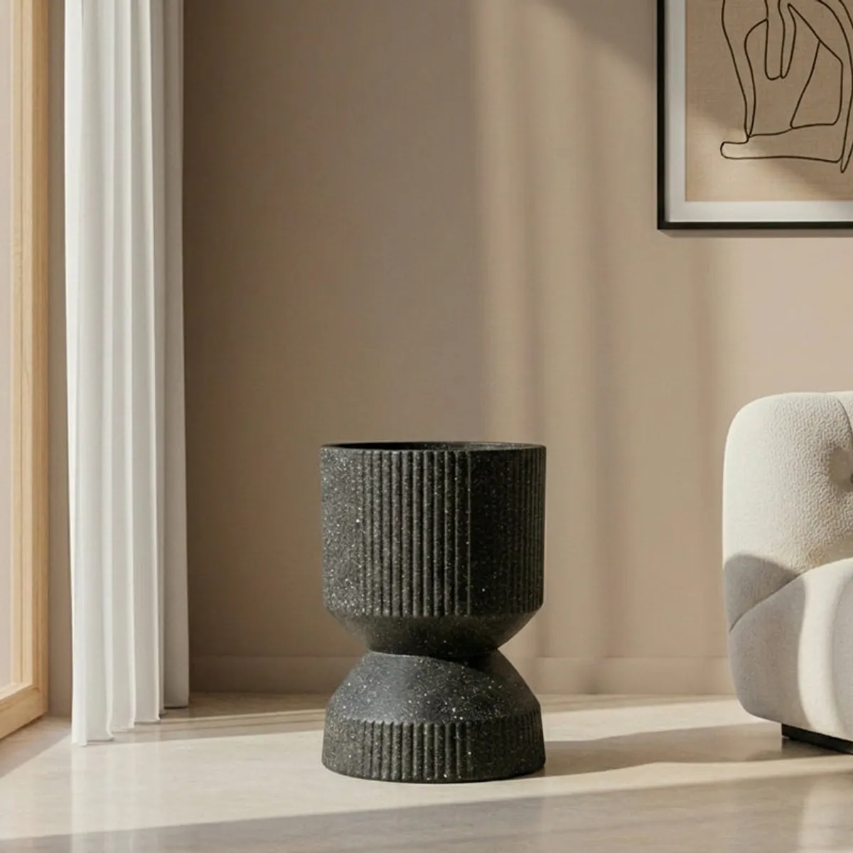 Black ribbed hourglass-shaped floor planter displayed beside a light armchair.