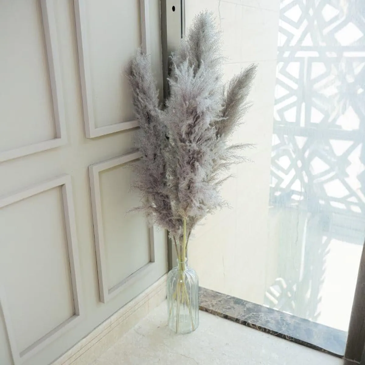 Grey pampas sticks arranged in a clear glass vase by a window