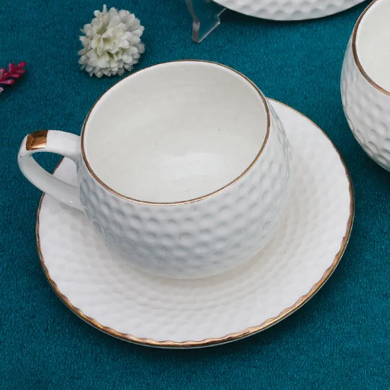 White textured cup and saucer with gold edging on a teal surface