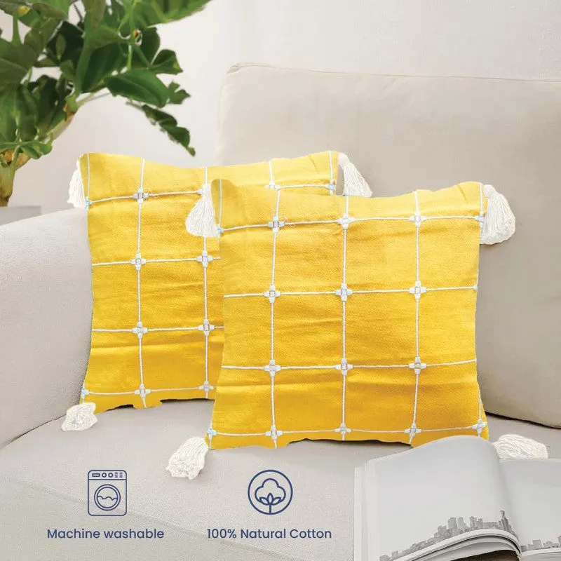 Two yellow cushion covers with white grid detailing and tassels on an armchair