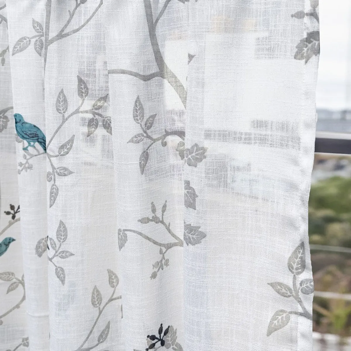 Translucent white curtain with grey leafy branches and blue bird motifs