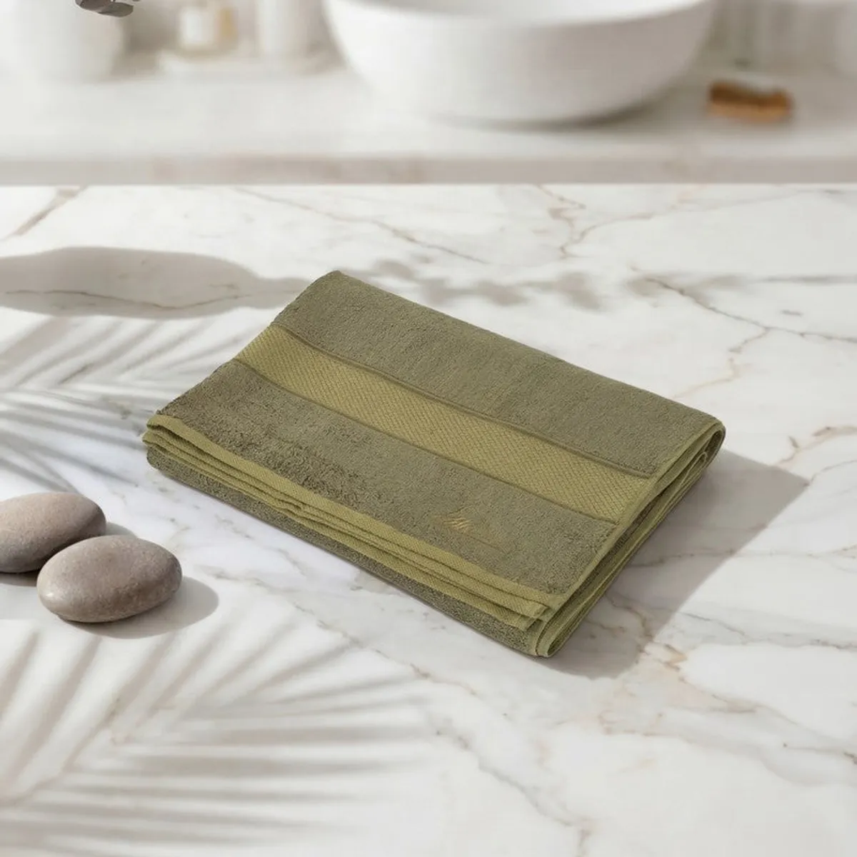 Folded olive green bath towel with contrasting border on a marble surface