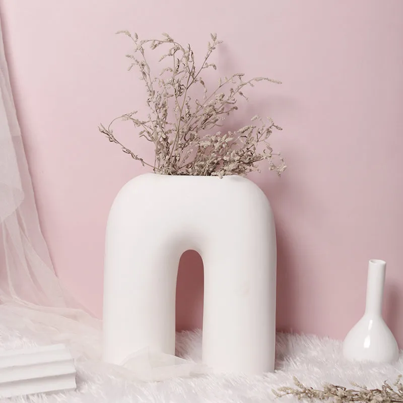 White sculptural arc vase with dried stems against a pink backdrop