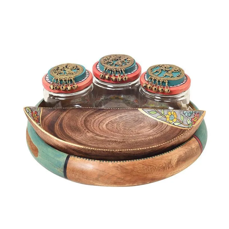 Front view of three ornate-lidded glass jars, wooden tray and floral-accented platter.