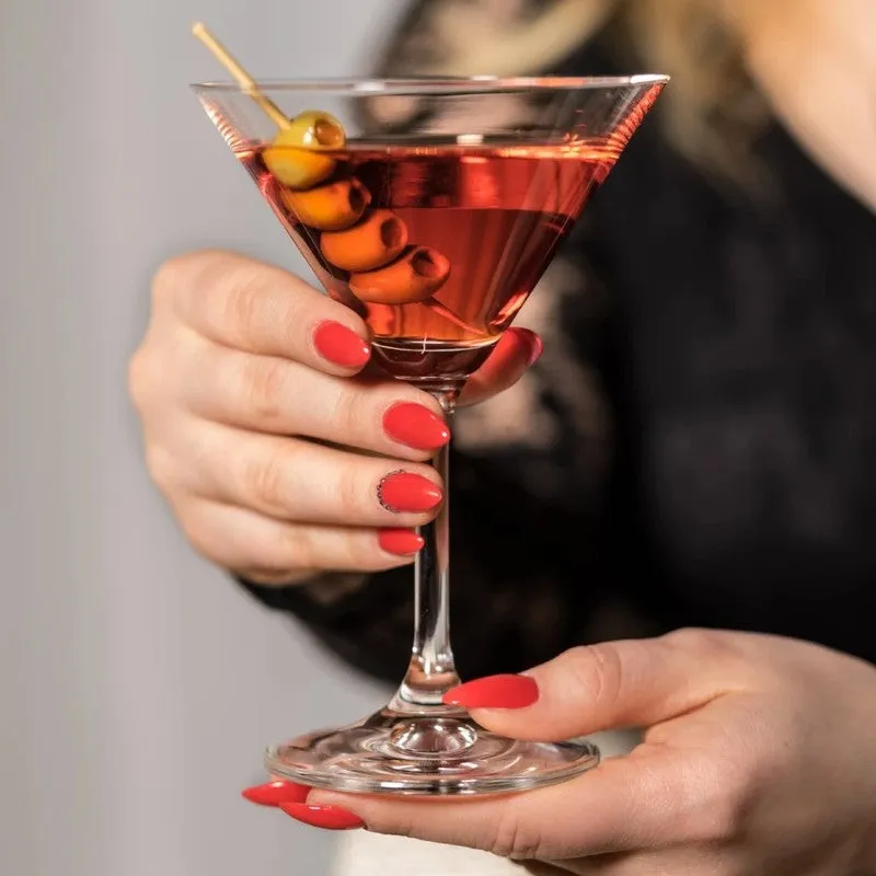 Hand holding a clear stemmed cocktail glass with a red drink and olives