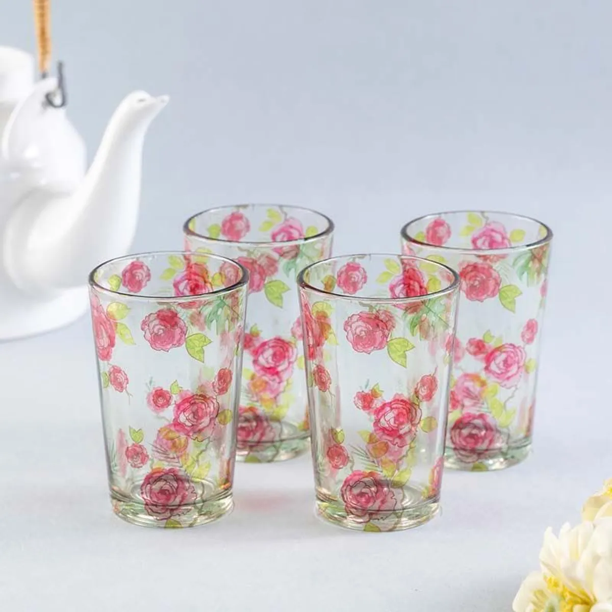 Four clear floral chai glasses arranged together with pink roses and green leaves
