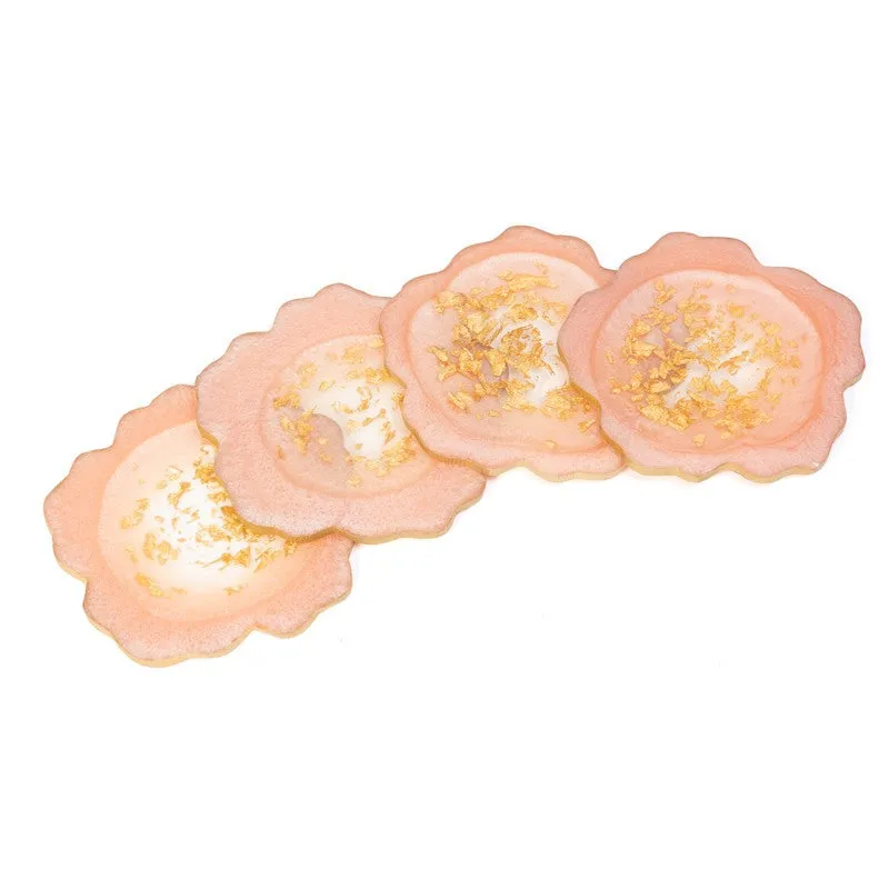 Four peach-pink coasters with gold detailing arranged on a white background