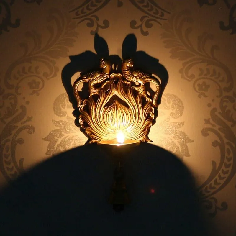 Lit gold wall hanging diya casting a large decorative shadow on the wall