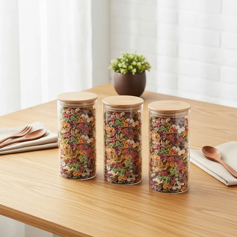 Three clear glass storage jars with bamboo lids filled with colourful dry food on a wooden table.