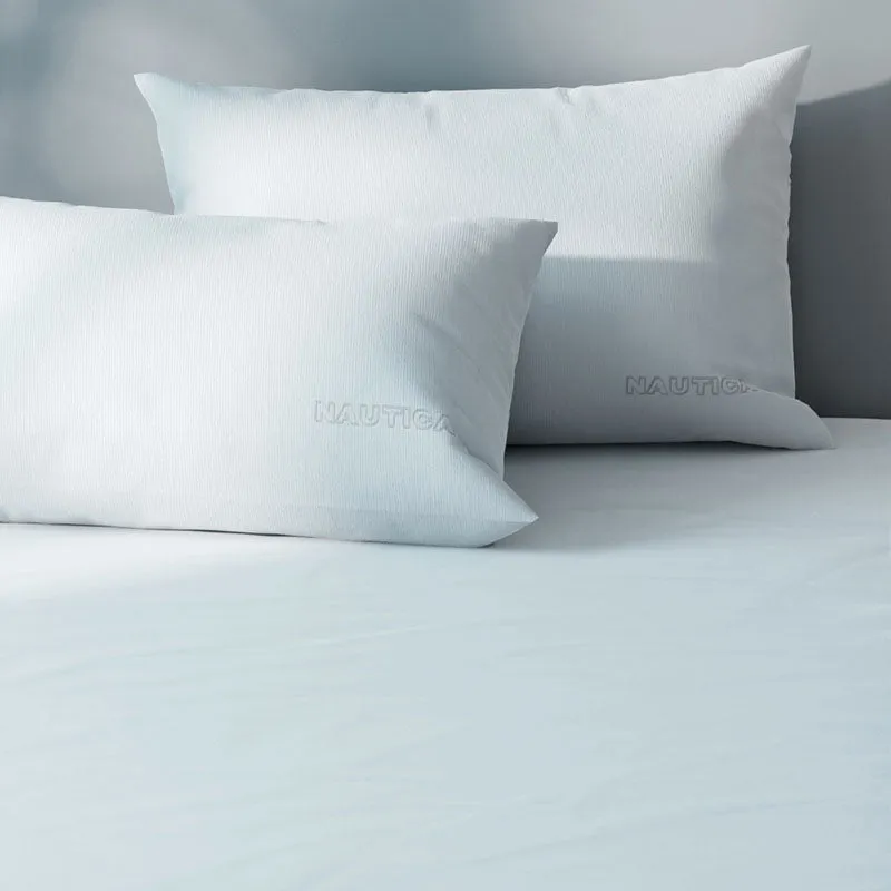 Close-up of white bedding with subtle ribbed texture and branded pillows