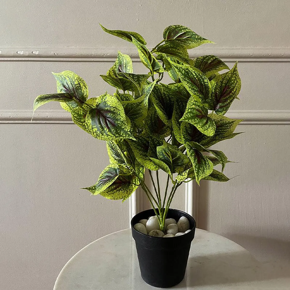 Green speckled faux coleus plant in a black pot with decorative stones