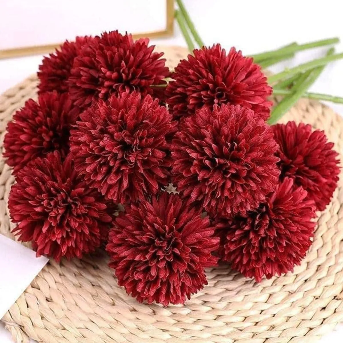Six deep red artificial chrysanthemum blooms displayed on a woven mat
