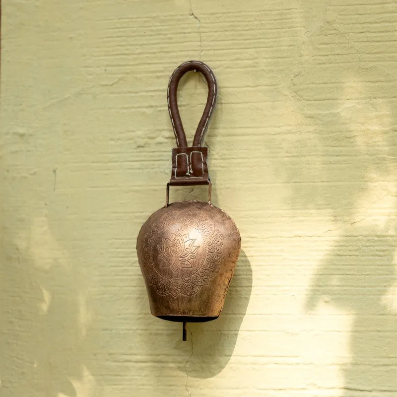 Copper hanging bell with a floral motif displayed on a pale wall.