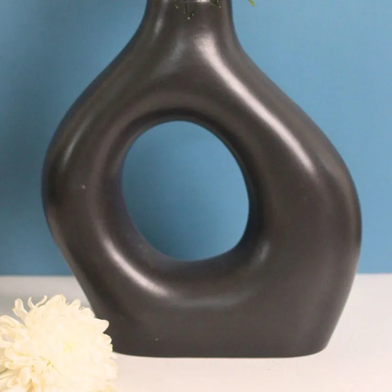 Lower close-up of a black sculptural vase with a white flower on the table