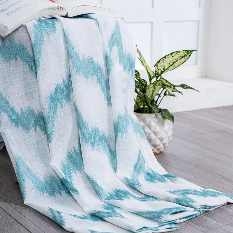 Blue and white patterned curtain draped over a surface beside a plant.