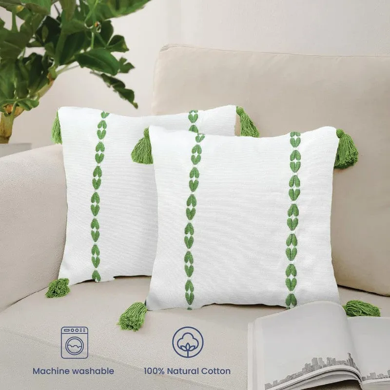 Two white cushion covers with green motifs and tasselled corners on a beige sofa