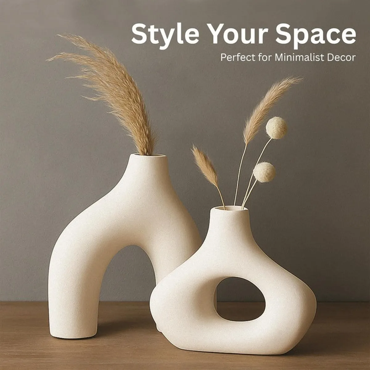 Two white sculptural vases styled with dried grass stems on a wooden surface.