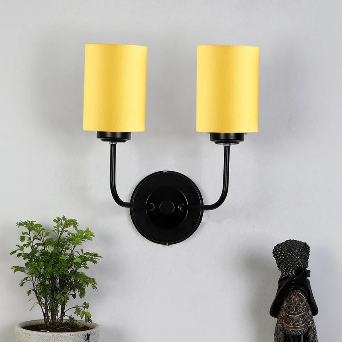 Yellow twin-shade wall lamp with black iron base against a white wall
