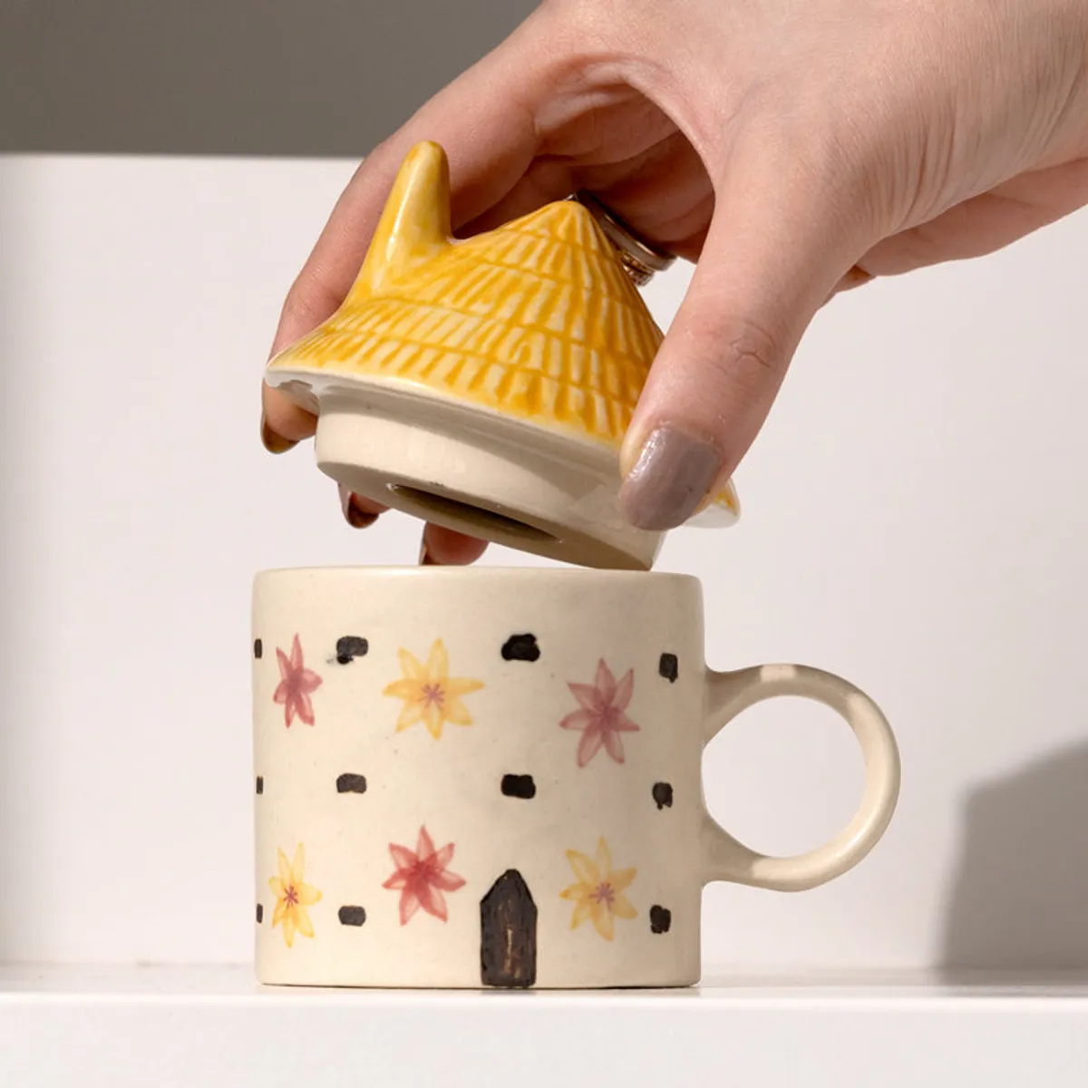 Hand lifting the yellow lid from a floral ceramic cottage mug
