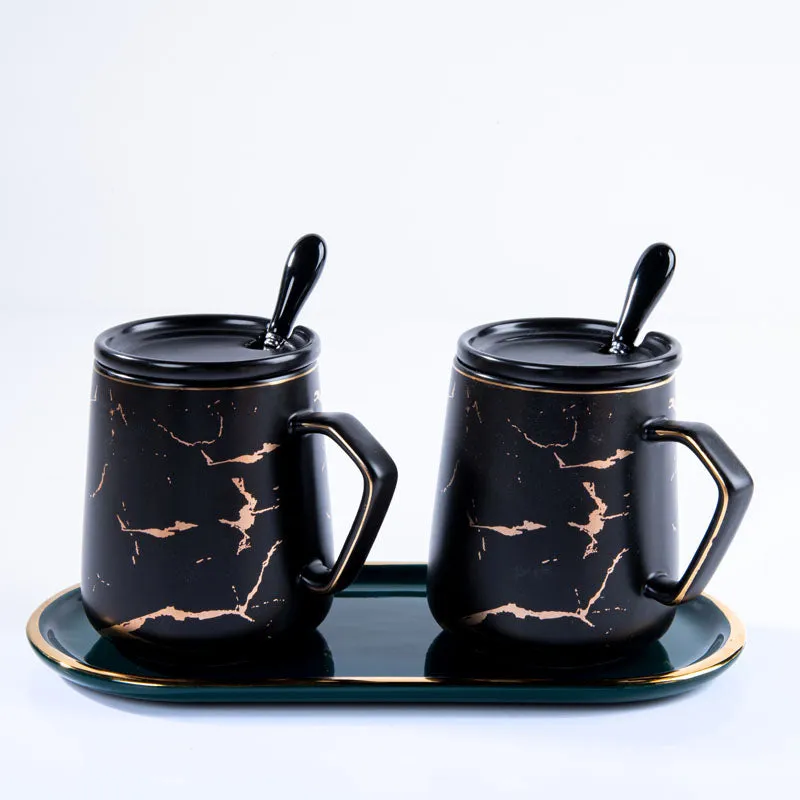 Two black patterned mugs with lids displayed on a green tray