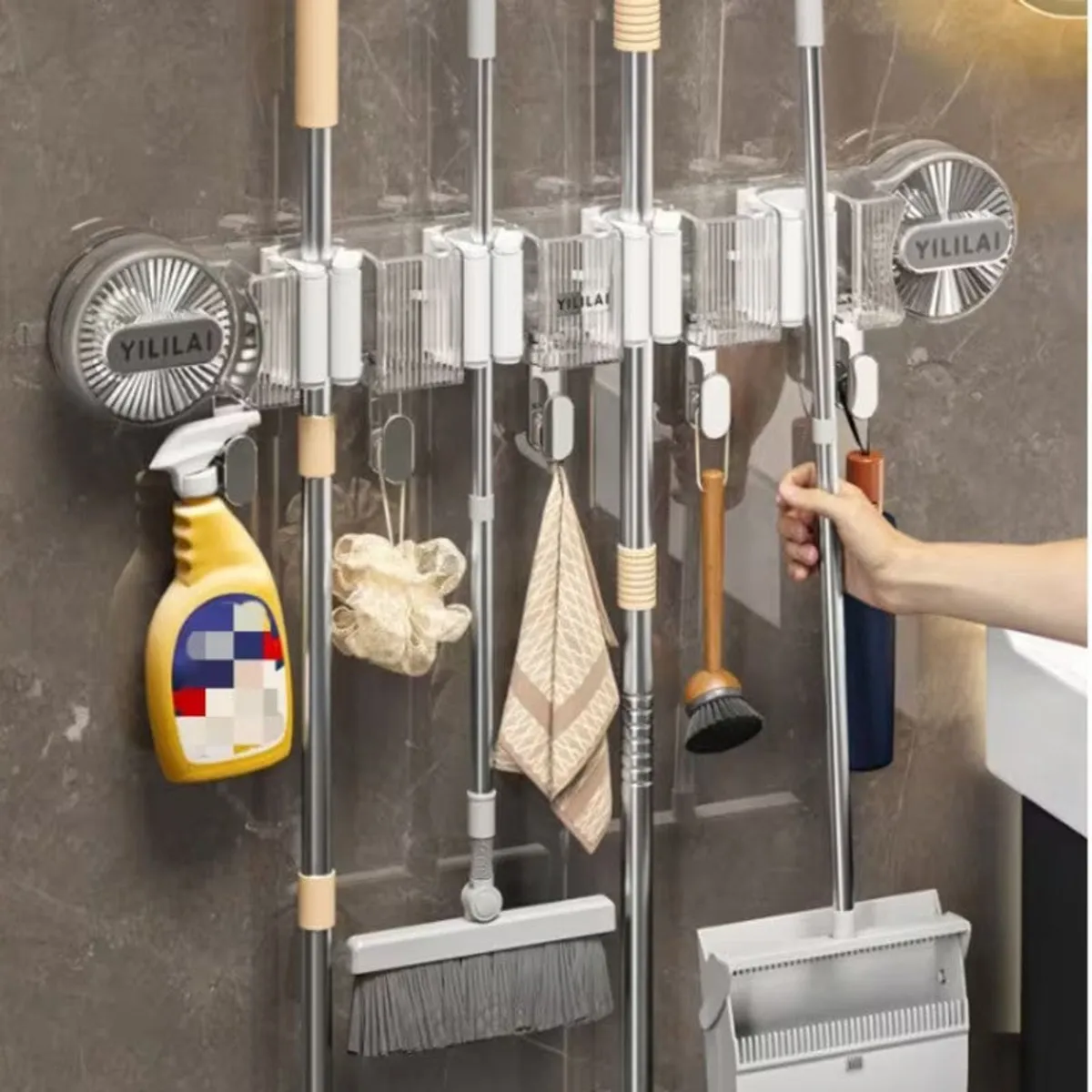 Wall-mounted transparent organiser storing mops, spray bottle and cleaning accessories