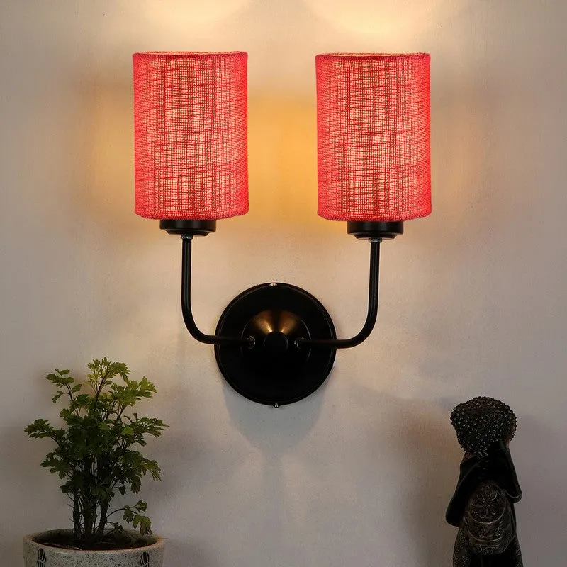Lit pink twin wall lamp with black iron arms and round wall plate