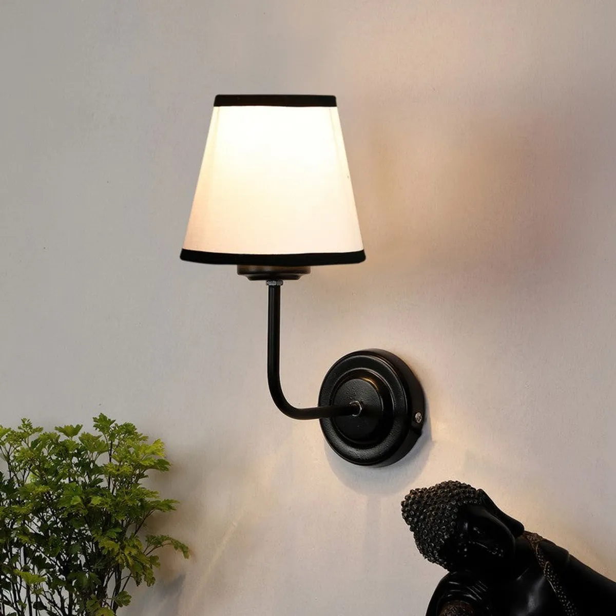 Lit wall lamp with white shade and black iron mount on a pale wall