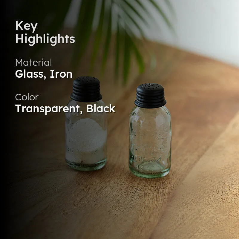 Two transparent glass shakers with black lids on a wooden table