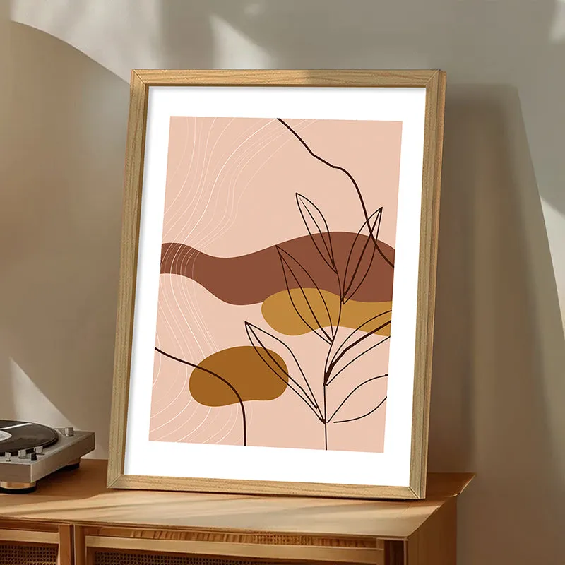 Gold-framed abstract botanical print leaning on a wooden cabinet in soft sunlight