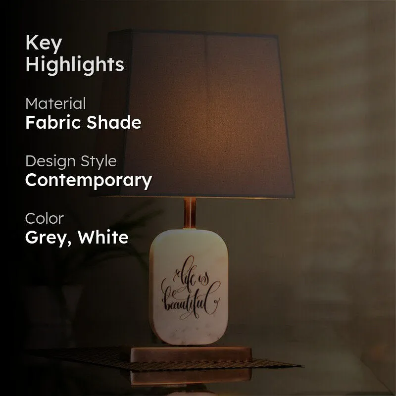 Lit grey and white table lamp with copper-toned base in a styled setting