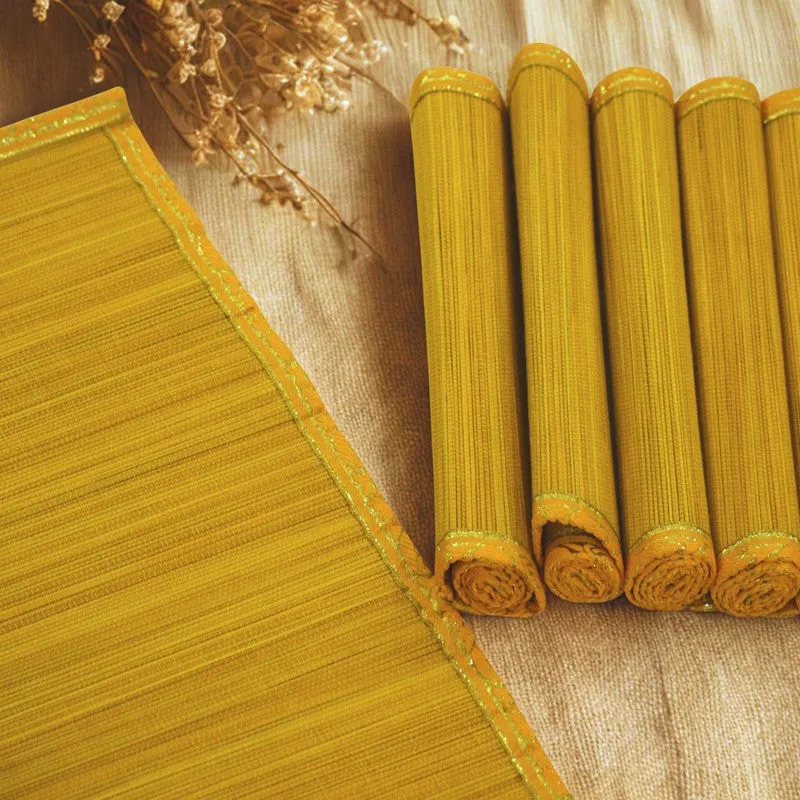 Close-up view of yellow mats showing their textured surface and zari borders