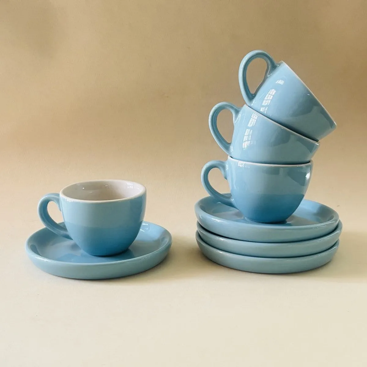 Blue ceramic cup and saucers displayed against a warm beige background