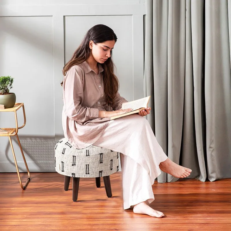 Person seated on a black-and-white patterned ottoman in a room